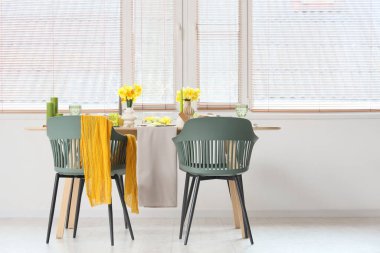 Aydınlık odada pencerenin yanında narsis çiçekleri olan güzel bir masa.