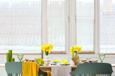 Aydınlık odada pencerenin yanında narsis çiçekleri olan güzel bir masa.