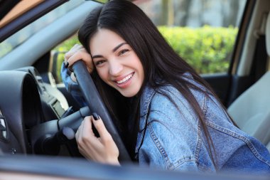 Mutlu genç bir kadın arabada direksiyona sarılıyor, yakın plan.