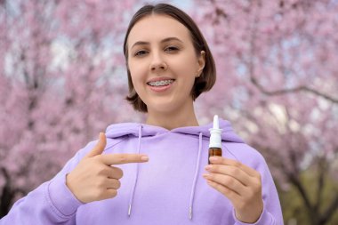 Alerjik genç kadın parktaki damlaları işaret ediyor, yakın plan.