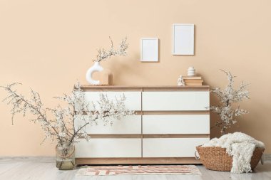 Çiçek açan dalları ve bej duvarın yanındaki sepeti olan çekmeceler.