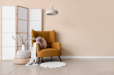 Oturma odasının içinde koltuk, katlanır perde ve vazoda çiçek açan dallar.