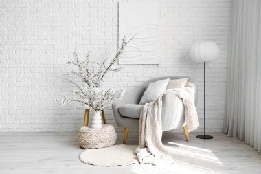 Gri koltuğu, lambası ve vazolarında çiçek açan dalları olan oturma odasının içinde.