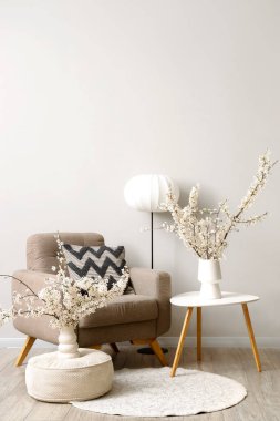 Gri koltuklu, masalı ve vazolarında çiçek açan dalları olan oturma odasının içinde.