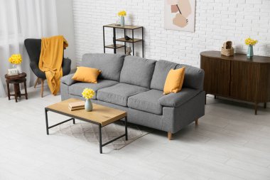 Rahat kanepe, şifonyer, sehpa ve narsis çiçekleri oturma odasındaki beyaz tuğla duvara karşı.