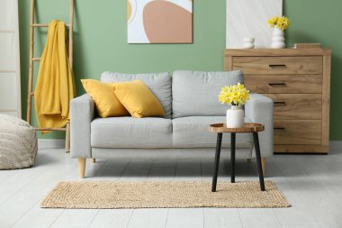 Soyunma odası, kahve masası ve yeşil duvarlı narsist çiçekli rahat bir kanepe.