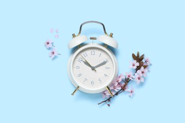 Alarm saati ve mavi arka planda çiçekler. Bahar geldi.