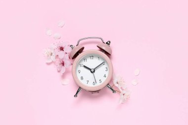 Alarm clock and flowers on pink background. Spring time