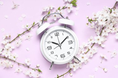 Çalar saat ve leylak arka planda çiçek açan dallar. Bahar geldi.