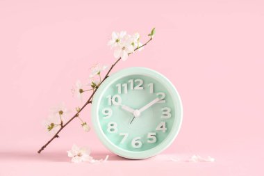 Alarm saati ve pembe arka planda çiçek açan bir dal. Bahar geldi.