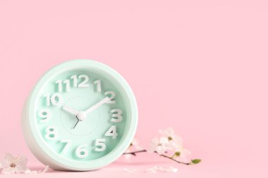 Alarm saati ve pembe arka planda çiçek açan bir dal. Bahar geldi.