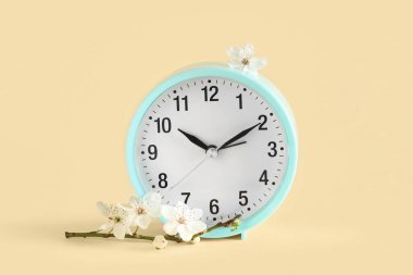 Çalar saat ve bej arka planda çiçekler. Bahar geldi.