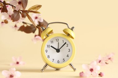 Alarm saati ve bej arka planda çiçek açan bir dal. Bahar geldi.
