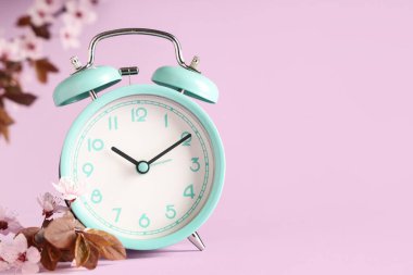 Alarm saati ve pembe arka planda çiçek açan dallar. Bahar geldi.