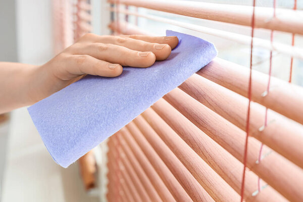 Женская ручная уборка жалюзи на окне в номере, крупный план