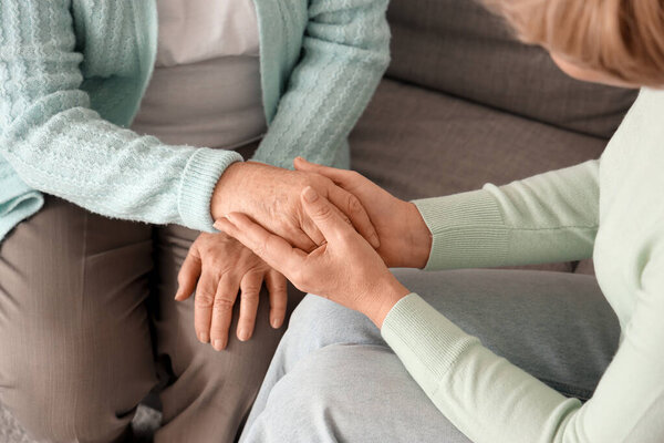 Зрелая женщина с матерью, держащей за руки диван дома, крупным планом