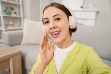 Evde diş teli takan kulaklıklı genç bir kadın var.