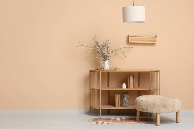 Oturma odasındaki bej duvarın yanında içi puf, avize ve vazo dolu raflar.