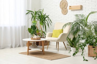 Beyaz tuğla duvarın yanında koltuk, masa ve çiçeklerle dolu bir oda.