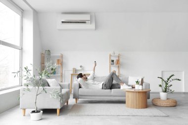 Yalancı genç adam oturma odasında klimayı açıyor.