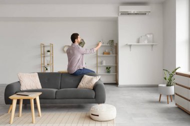 Genç bir adam oturma odasında klimayı açıyor.