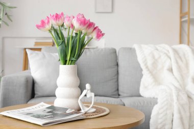 Oturma odasındaki masada lale, dergi ve heykelcikli vazo.