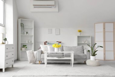 Aydınlık oturma odasının içinde gri kanepe, masa ve vazolarda nergisler.