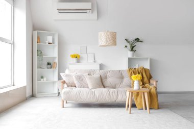 Kanepe, raf üniteleri ve vazolarda nergislerle aydınlık oturma odasının içinde.