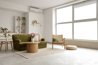 Yeşil kanepe, koltuk ve bitkilerle aydınlık oturma odasının içinde.