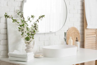 Çiçek açan dalları olan bir vazo ve banyoda beyaz tuğla duvarın yanındaki masada lavabo.