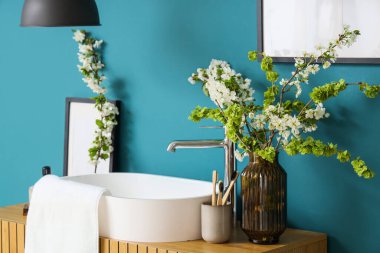 Çiçek açan dalları, diş fırçaları ve banyodaki mavi duvarın yanında lavabosu olan vazo.