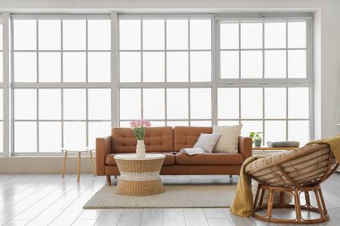 Oturma odasının içinde kahverengi kanepe, koltuk ve vazoda laleler.