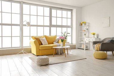 Sarı kanepe, koltuk ve bahar çiçekleriyle oturma odasının içinde.