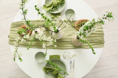 Tabakları, mumları ve çiçek açan ağaç dalları olan zarif bir masa.