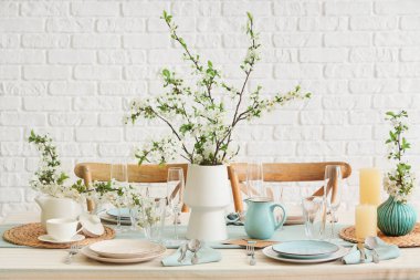 Tabakları, bardakları ve çiçek açan ağaç dalları olan zarif bir masa.