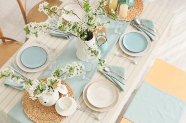 Tabakları, bardakları ve çiçek açan ağaç dalları olan zarif bir masa.