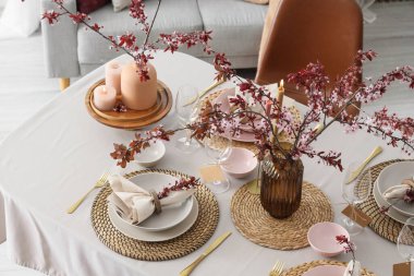 Tabakları, yanan mumları ve çiçek açan ağaç dalları olan zarif bir masa.