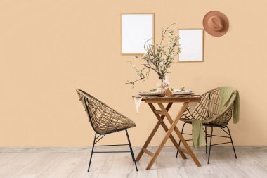 Tabaklar, bardaklar ve bej duvarın yanında çiçek açan ağaç dalları olan zarif bir masa.