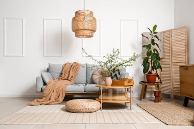 Oturma odasının içinde gri kanepe, masa ve vazoda çiçek açan dallar.