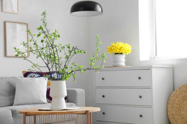 Aydınlık oturma odasındaki masada çiçek açan dalları olan vazo.