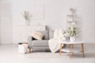 Şifoniyerli kanepe, sehpa ve oturma odasındaki beyaz tuğla duvarın yanında çiçek açan dalların olduğu bir vazo.