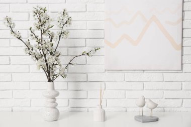 Oturma odasındaki beyaz tuğla duvarın yanındaki dolapta dekoru olan beyaz çiçek açan bir vazo.