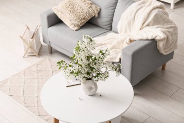 Oturma odasındaki kanepenin yanındaki sehpanın üzerinde açan beyaz dallardan oluşan bir vazo.