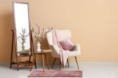 Ayna, sehpa ve oturma odasındaki bej duvarın yanında çiçek açan dallardan oluşan bir vazo.