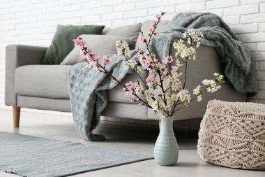 Oturma odasındaki kanepenin yanındaki yerde çiçek açan bir vazo.