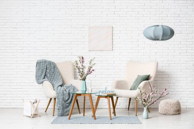 Kahve masalı koltuklar, farklı dekorlar ve oturma odasındaki beyaz tuğla duvarın yanında çiçek açan vazolar.