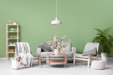 Koltuklu kanepe, sehpa ve oturma odasındaki yeşil duvarın yanında açan dallardan oluşan vazo.