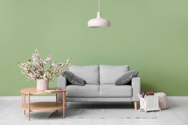 Kahve masalı kanepe, avize ve yeşil duvarın yanında çiçek açan vazo oturma odasında.