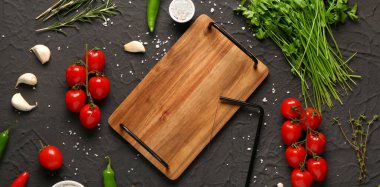 Ahşap mutfak tahtası, taze sebzeler, koyu arkaplanda otlar ve baharatlar.