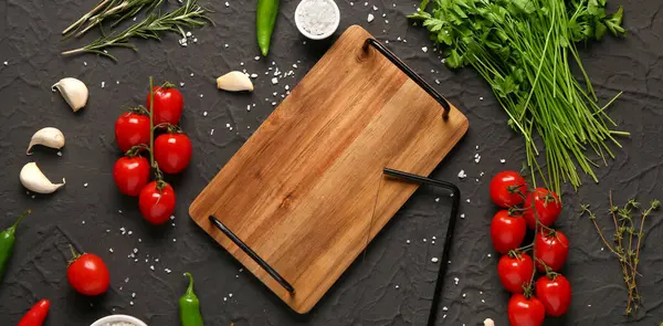 Ahşap mutfak tahtası, taze sebzeler, koyu arkaplanda otlar ve baharatlar.